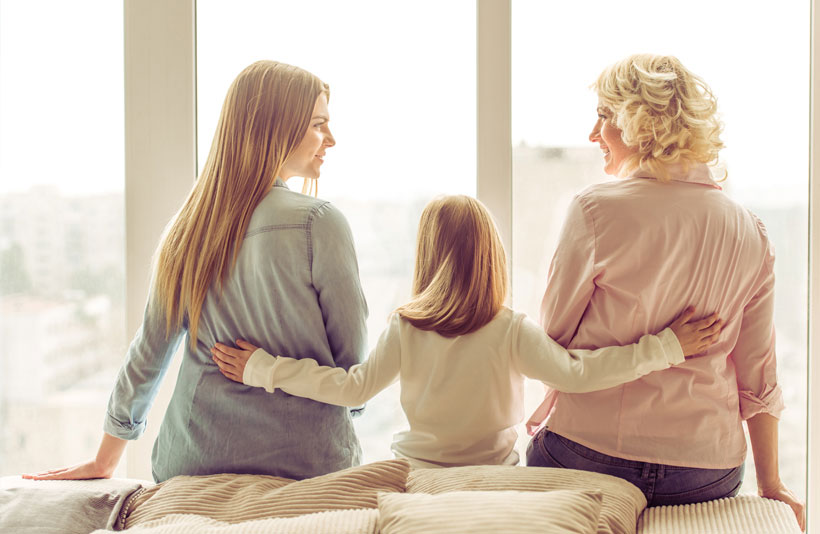 Three women sitting on a bed. Grandmother, daughter and granddaughter