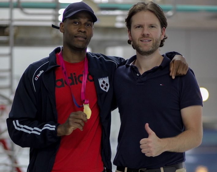 Swimmer Masai Zebechaka holding his gold medal at the pool with Sports Chiropractic Dr Wesley Trowse standing next to him